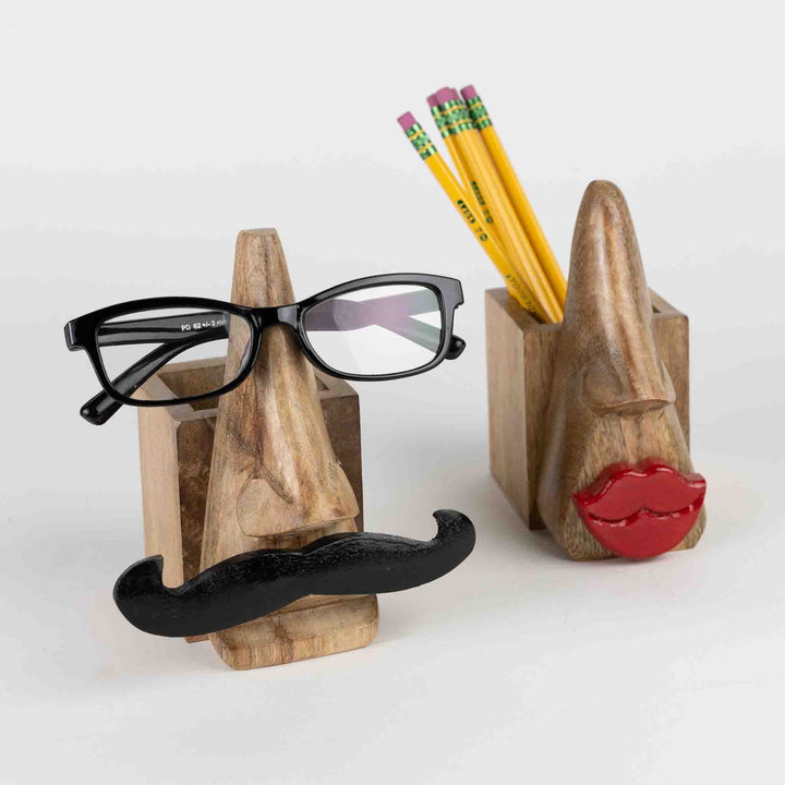 Handcrafted eyeglass and pencil holder made from sustainably sourced mango wood. Features a playful mustache face design in natural and black finishes. Measures 5.5" high with a 2.5" square base. Eco-friendly and easy to clean.